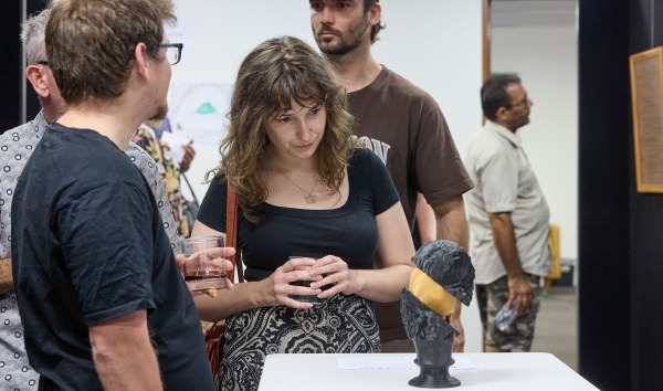 A woman examining a sculpture at an exhibition while other people look around