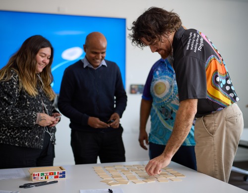 People standing around a table with one man pointing towards small cards