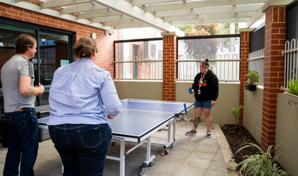 Three people around a table tennis table holding paddles