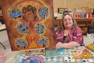 A woman displaying a piece of aboriginal artwork that she has made