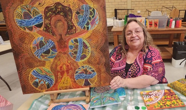 A woman displaying a piece of aboriginal artwork that she has made