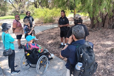 A man giving a talk to a group of people in a park for the MDW tour