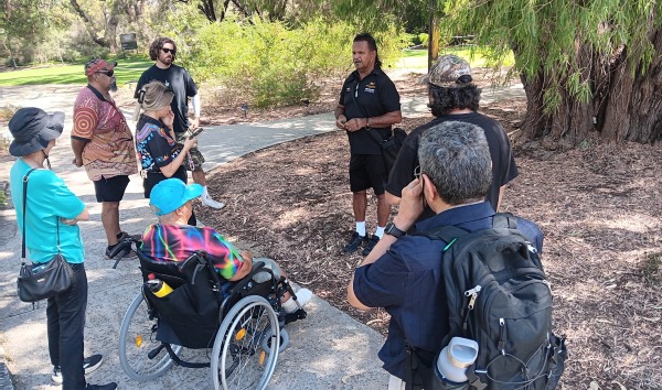 A man giving a talk to a group of people in a park for the MDW tour