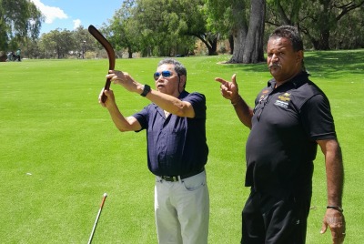Two men standing on the grass with one of them demonstrating how to use a boomerang