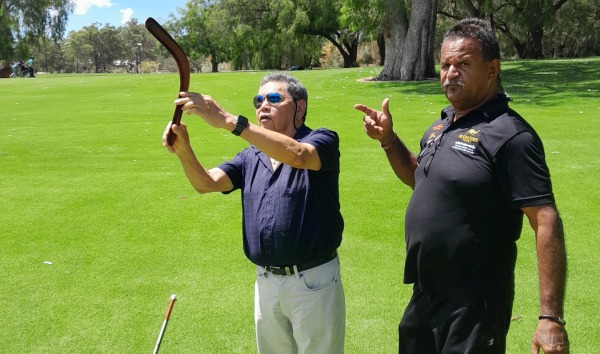 Two men standing on the grass with one of them demonstrating how to use a boomerang