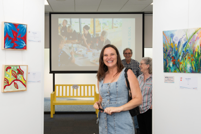 A woman smiling at the camera in between some paintings at the Heart and Soul Exhibition