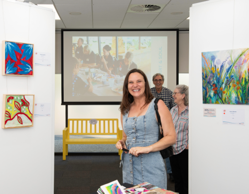 A woman smiling at the camera in between some paintings at the Heart and Soul Exhibition