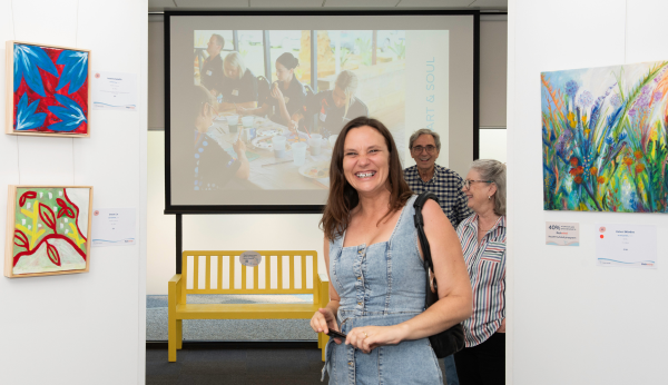 A woman smiling at the camera in between some paintings at the Heart and Soul Exhibition