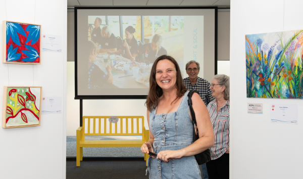 A woman smiling at the camera in between some paintings at the Heart and Soul Exhibition