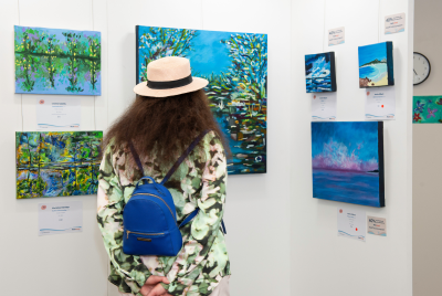 A woman looking at a collection of paintings from the Heart and Soul exhibition