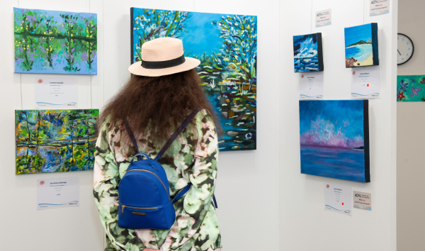 A woman looking at a collection of paintings from the Heart and Soul exhibition