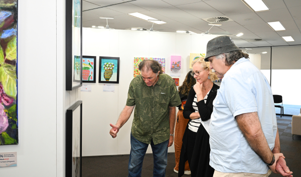 Two men and a woman looking at one of the paintings at the Heart and Soul Exhibition