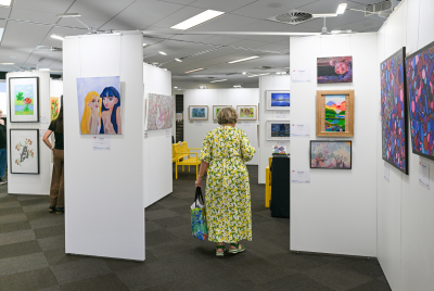 A woman walking among various paintings in the Heart and Soul Exhibition