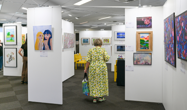 A woman walking among various paintings in the Heart and Soul Exhibition