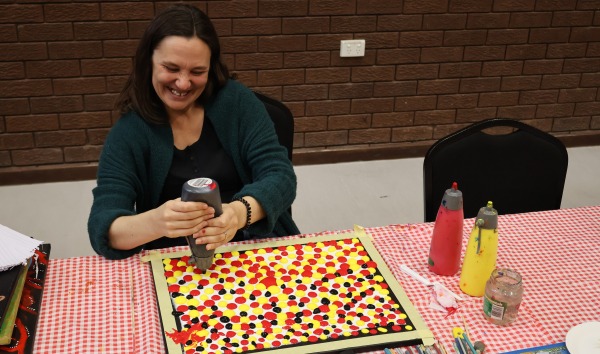A woman sitting at a table and making a piece of artwork