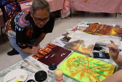 A woman bending over a table and painting as part of Heart and Soul
