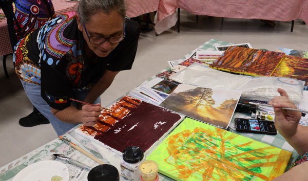A woman bending over a table and painting as part of Heart and Soul