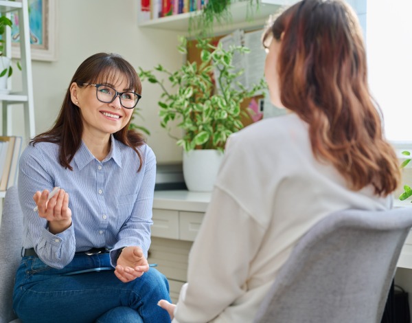 Two women sitting down and speaking with one another while smiling